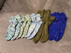 A collection of five pairs of hand knit socks in varying shades of purples, greens, and blues